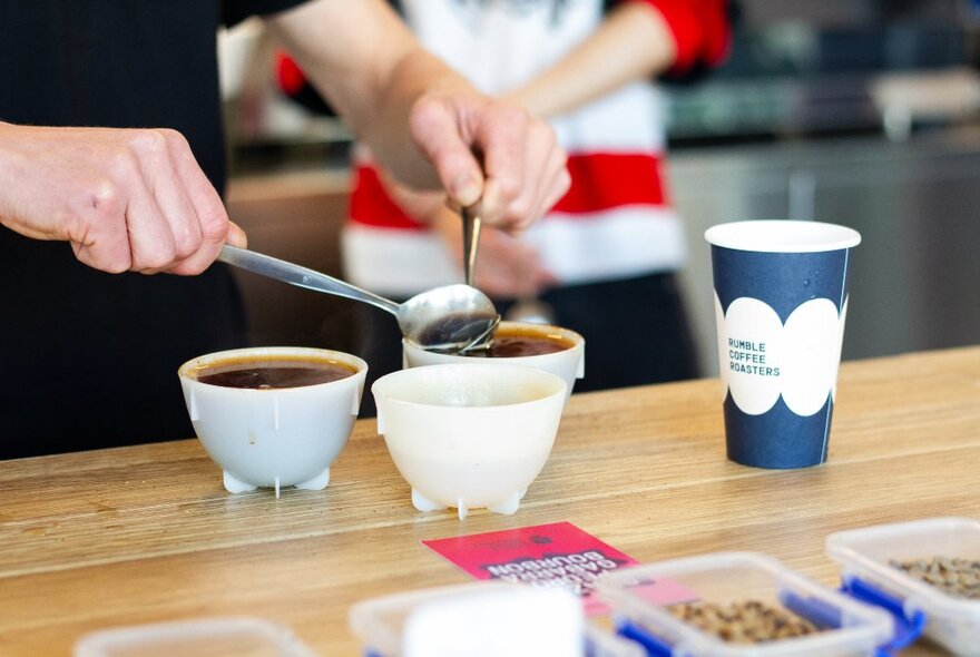 A person hosting a coffee cupping demonstration in a shop, pouring coffee into cups on a table.