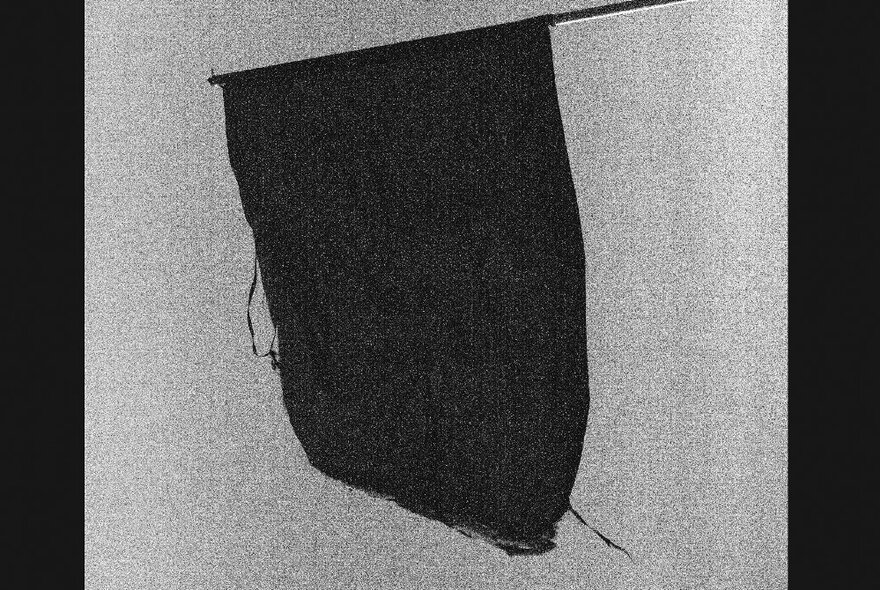 A dark piece of fabric hanging from a stick, like a makeshift flag, against a light coloured wall.