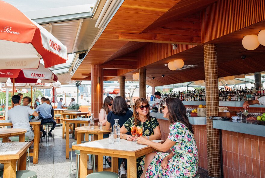 Two friends are sitting in a rooftop bar drinking cocktails