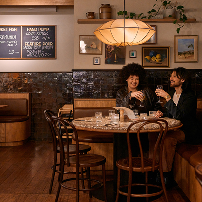 Two friends sitting at a pub table sharing a wine. 
