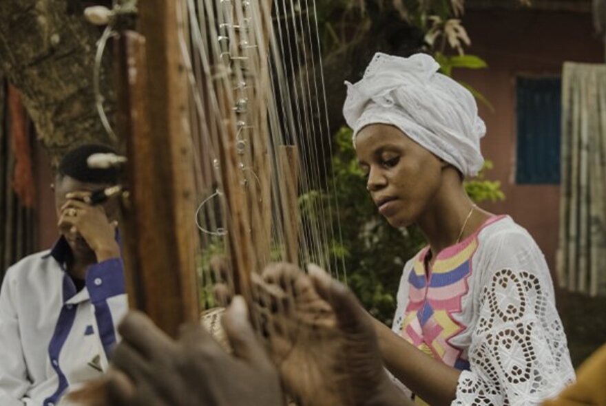 A still from an African film showing a traditionally dressed African woman playing the harp.
