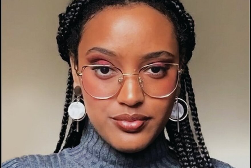 Head shot of author Tigest Girma, a young woman wearing glasses and dangling earrings, with braided black hair.