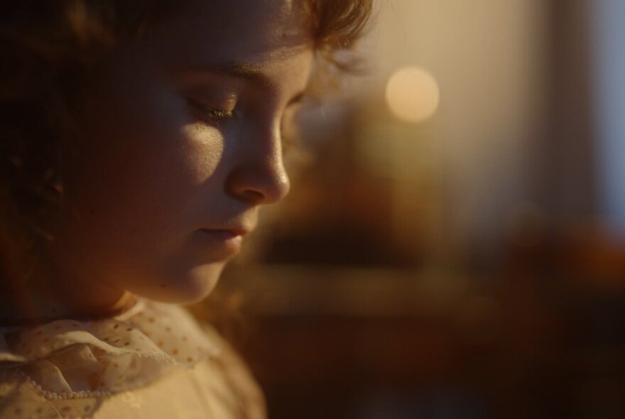 Closeup of a young woman's face looking pensive, her eyes looking down.