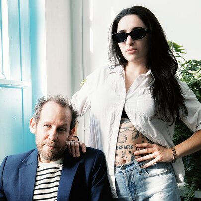 Singers Ben Lee (seated) and Georgia Maq standing beside him with her hand on her hip and sunglasses on.