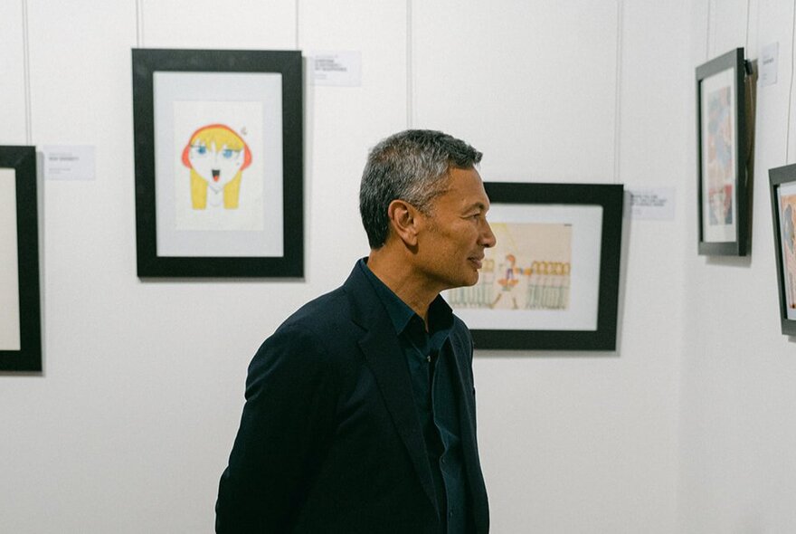 Man looking at framed artworks on a white gallery wall.