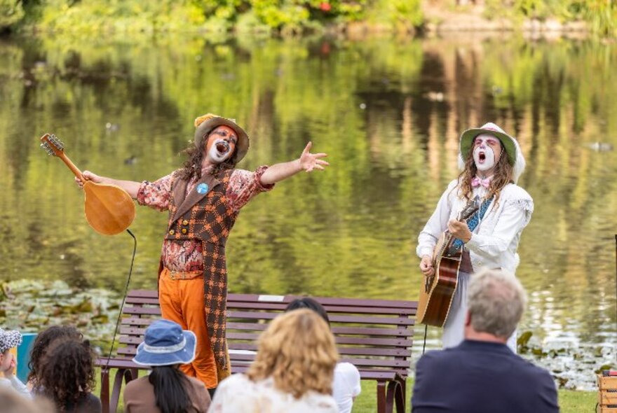 Two actors from Wind in the Willows singing in front of the lake at Royal Botanic Gardens, in front of an audience seated on the grass.