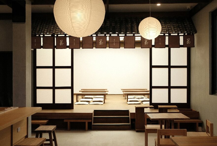 The interior of a Japanese Matcha store, with tables and chairs, and a raised platform with Japanese-style table seating behind Japanese paper screens.