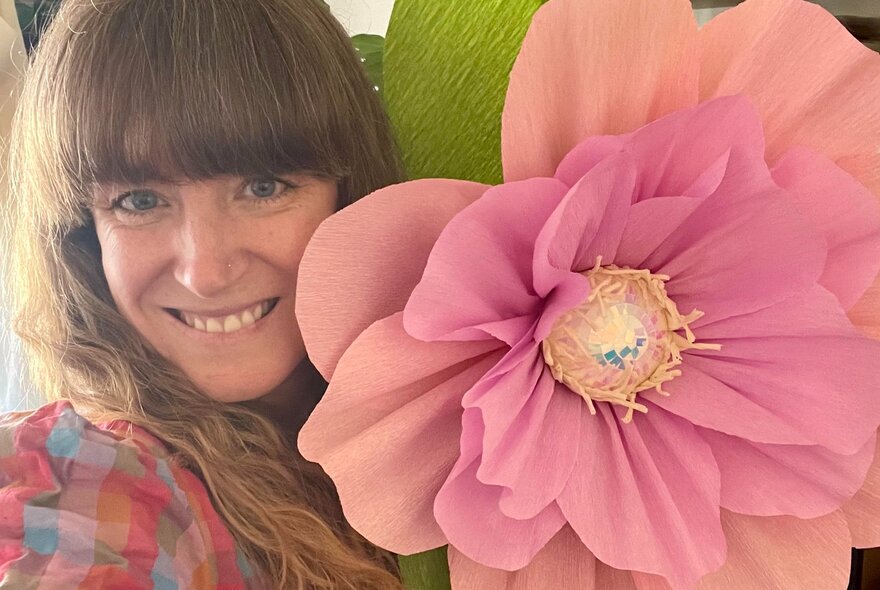 A woman smiling next to an oversized hand made paper flower.