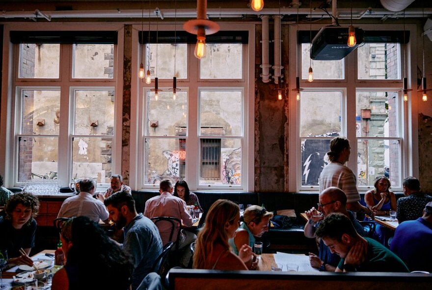 Interior of Chin Chin restaurant, with patrons seated at dining tables, with large windows looking out onto a laneway.