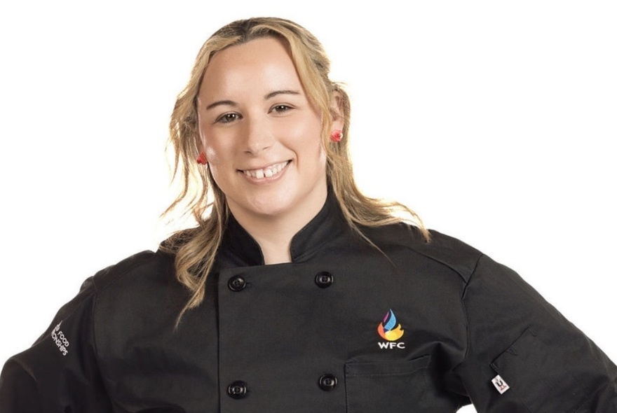 Portrait of a female chef with long blonde hair wearing a black chef's shirt, smiling.