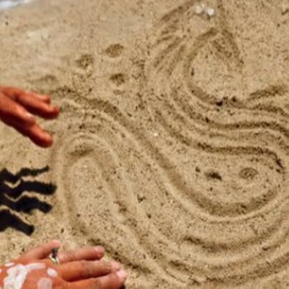 Hands with white paint drawing a snake in the sand.