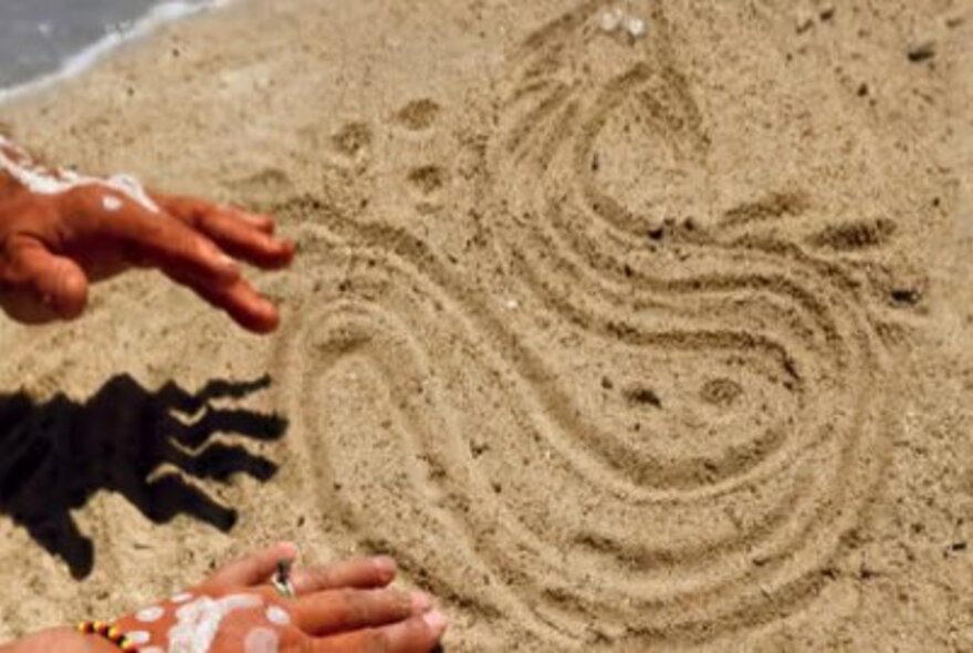 Hands with white paint drawing a snake in the sand.