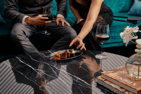 Hands of two people seated and about to select small chocolate delights from a plate. 