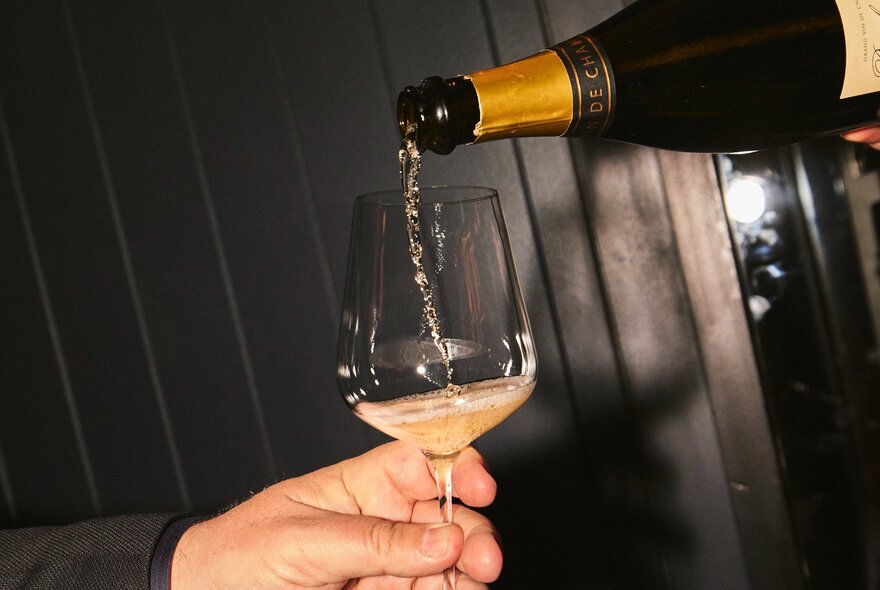 Sparkling wine being poured from a bottle into a glass in someone's hand.