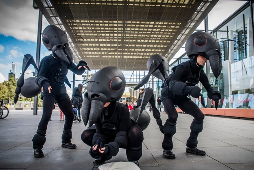 Three people in ant costumes outside in a covered walkway. 