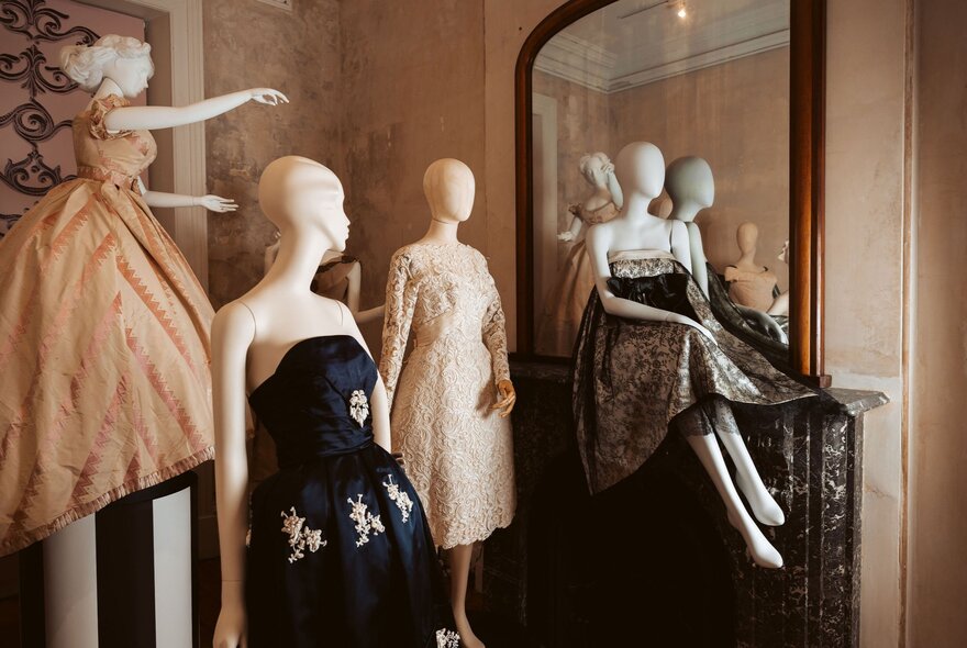 Evening frocks in neutral and black tones, on faceless clothing mannequins, displayed in an exhibition space.