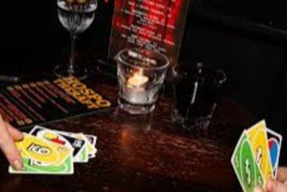 Hands playing the card game Uno, with drinks on a wooden table.