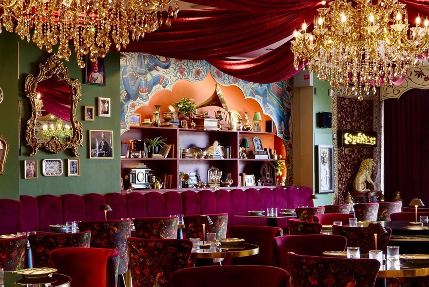 Opulent Indian restaurant with chandeliers, fabric swags, banquette seating and shelves with ornaments.