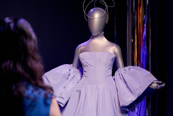 A woman looking at a mannequin wearing a light purple dress.