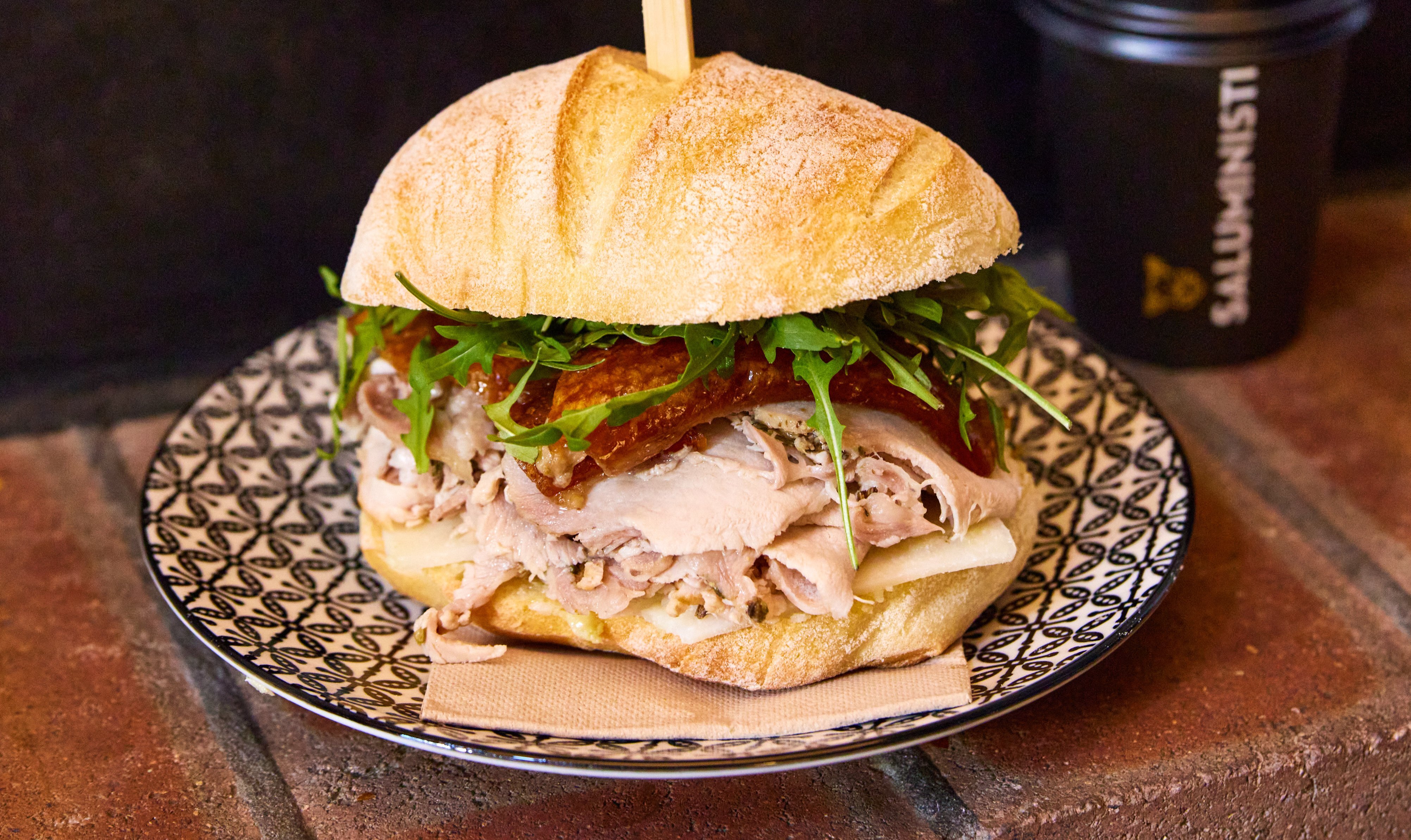 A close-up of a panini full of deli meat, cheese and rocket.