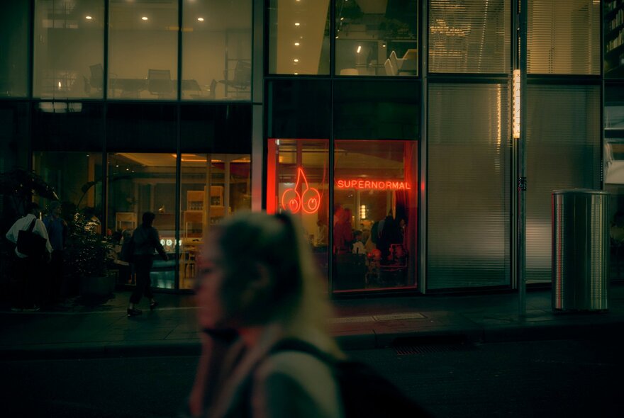Exterior of Supernormal restaurant on a winter's night, with pedestrians walking past, the view though the window is of a warm inviting space. 
