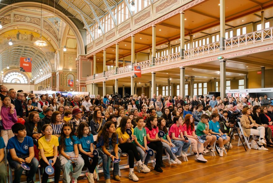A seated audience of children inside the Royal Exhibition Building, the domed roof visible behind them.