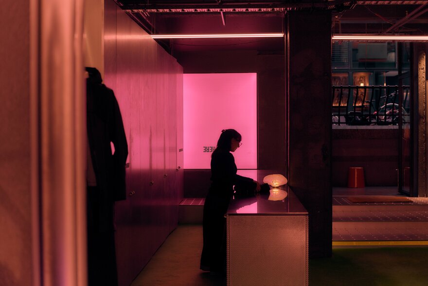Interior of Up There retail space features minimalist design elements, including a bright pink glowing wall and a central counter.