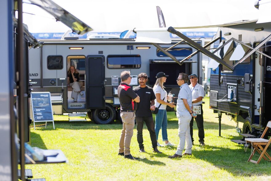 Five people looking at three caravans on display.