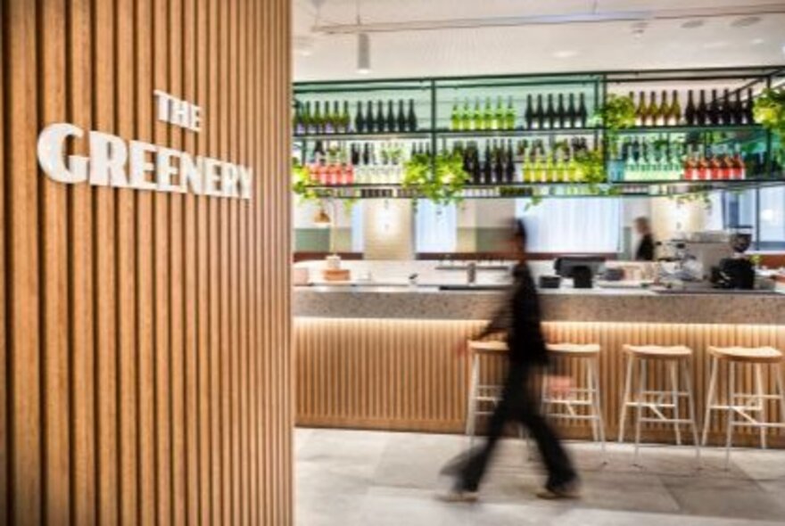 A view of the bar from the wood-lined front entrance of a cafe/restaurant, the blurred shadow of a person walking through.