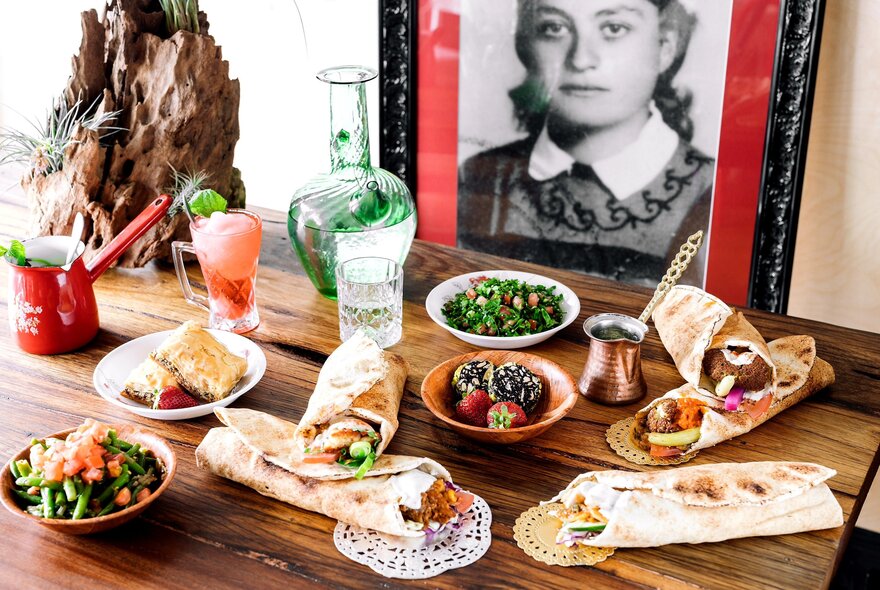 A framed black and white photograph of a young woman from Beirut with a selection of Lebanese food and drink on the table in front of it.