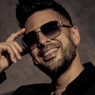 Smiling bearded man wearing sunglasses, his finger to his temple.