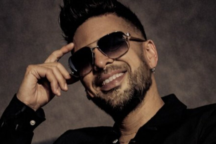 Smiling bearded man wearing sunglasses, his finger to his temple.