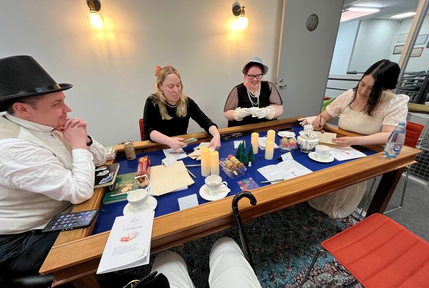 Four people in Regency-era themed costumes seated at a table.