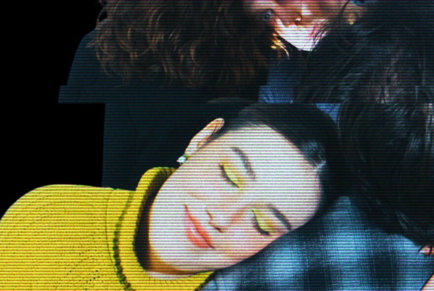 A woman's smiling serene face, her eyes closed, resting her head on the shoulder of another person who is out of view.
