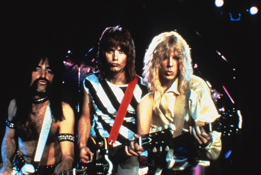 A still from the film, This is Spinal Tap, showing three 80s rockers on stage with their electric guitars, big hair and big lips.