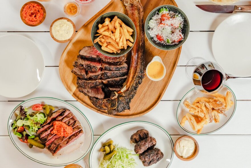 Overhead view of meat dishes including sliced steak and rissoles with chips and salad.