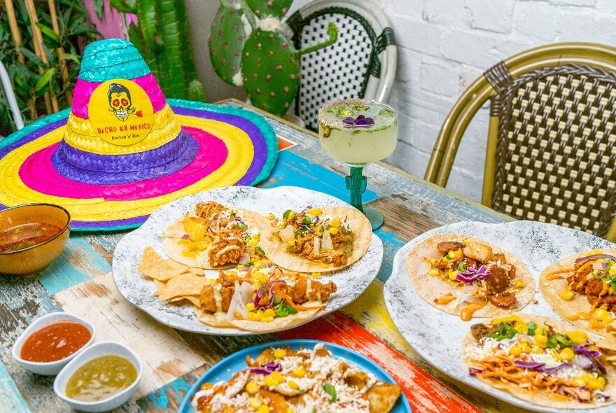 A table with taco share plates, a margarita and a colourful sombrero placed on top.