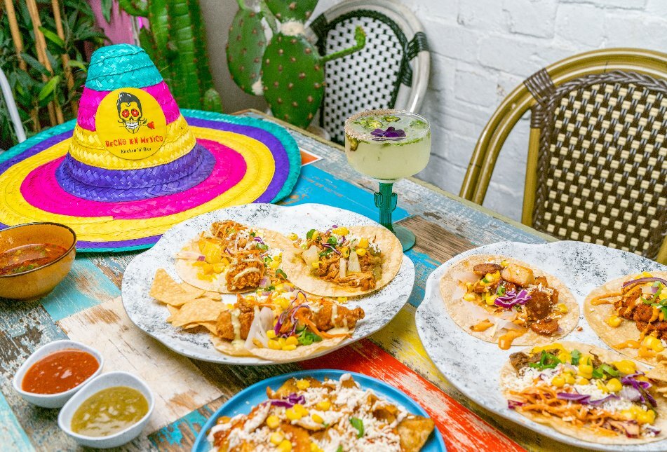 A table with taco share plates, a margarita and a colourful sombrero placed on top.