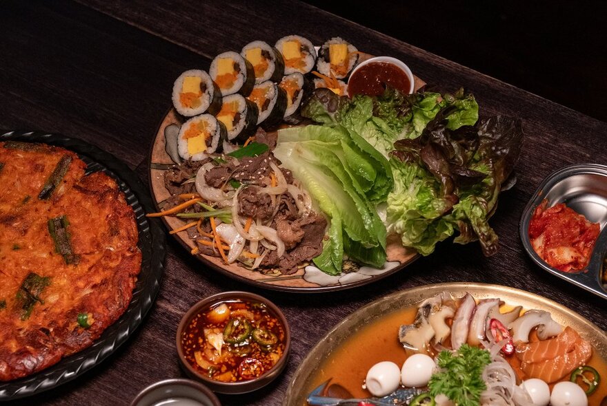 A table set with korean dishes including gimbap and kimchi pancake.