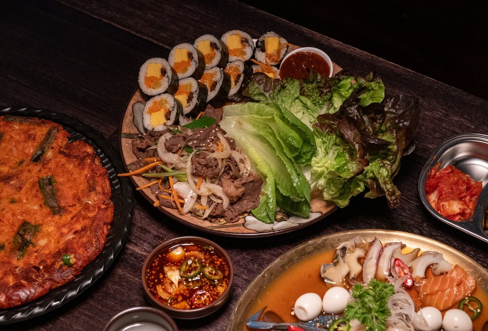 A table set with korean dishes including gimbap and kimchi pancake.