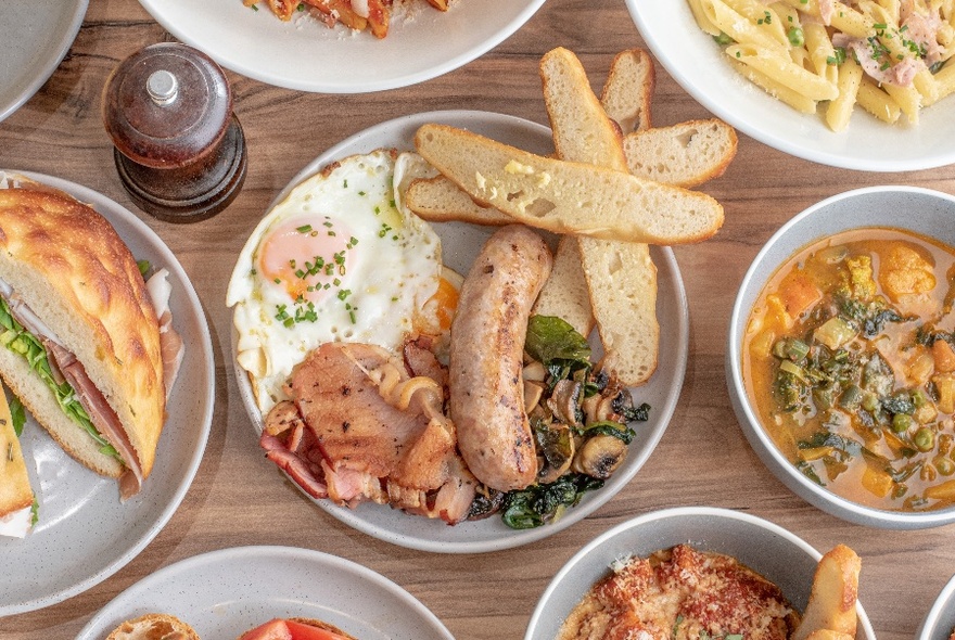 Display of dishes including egg and sausage breakfast, filled roll and bowls of pasta.