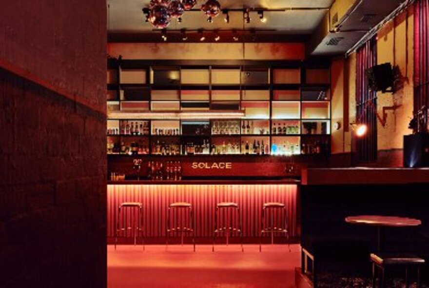 The interior of Solace Bar with a red glowing bar and stools and warm timber finishes. 