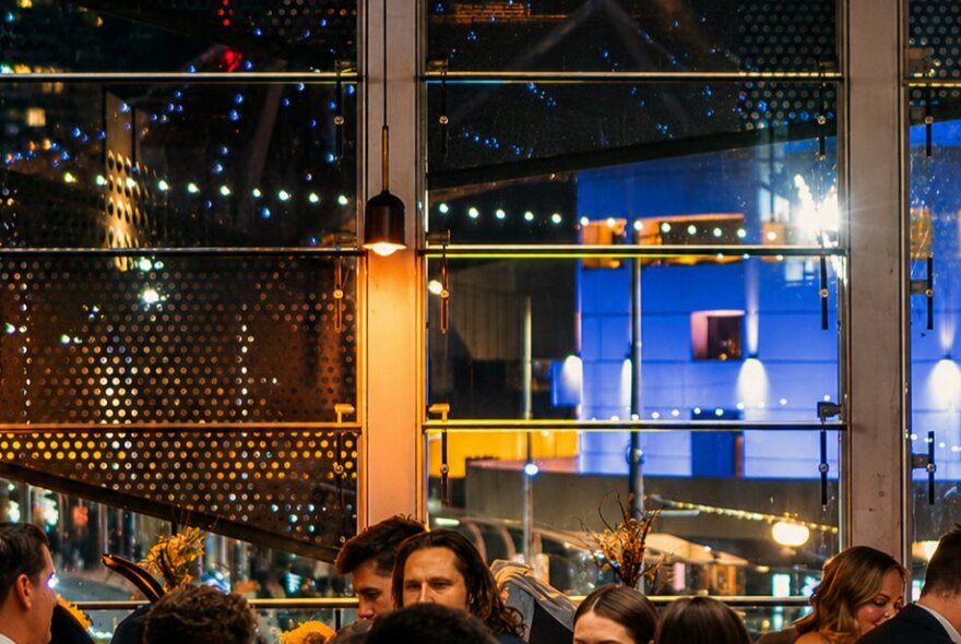 Dining space at Taxi Kitchen, showing the large wall of windows and night views into Fed Square and other buildings.