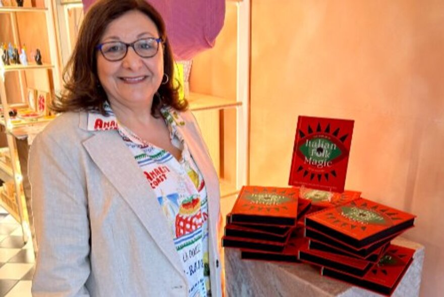 Woman standing next to a stack of books with red covers in a gift shop.