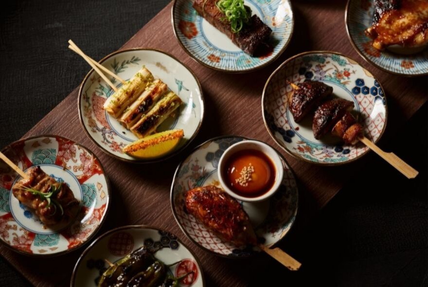 An array of Japanese food presented in small dishes, seen from above on a narrow wooden table.