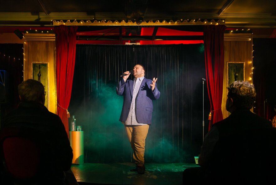 A man singing in front of an audience in a small theatre setting. 