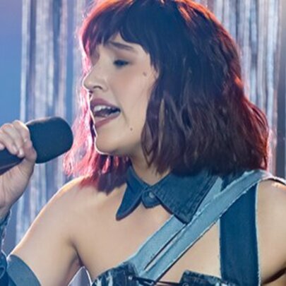 Singer CYNTA singing on stage in front of a silver stage curtain.