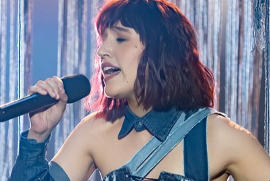 Singer CYNTA singing on stage in front of a silver stage curtain.