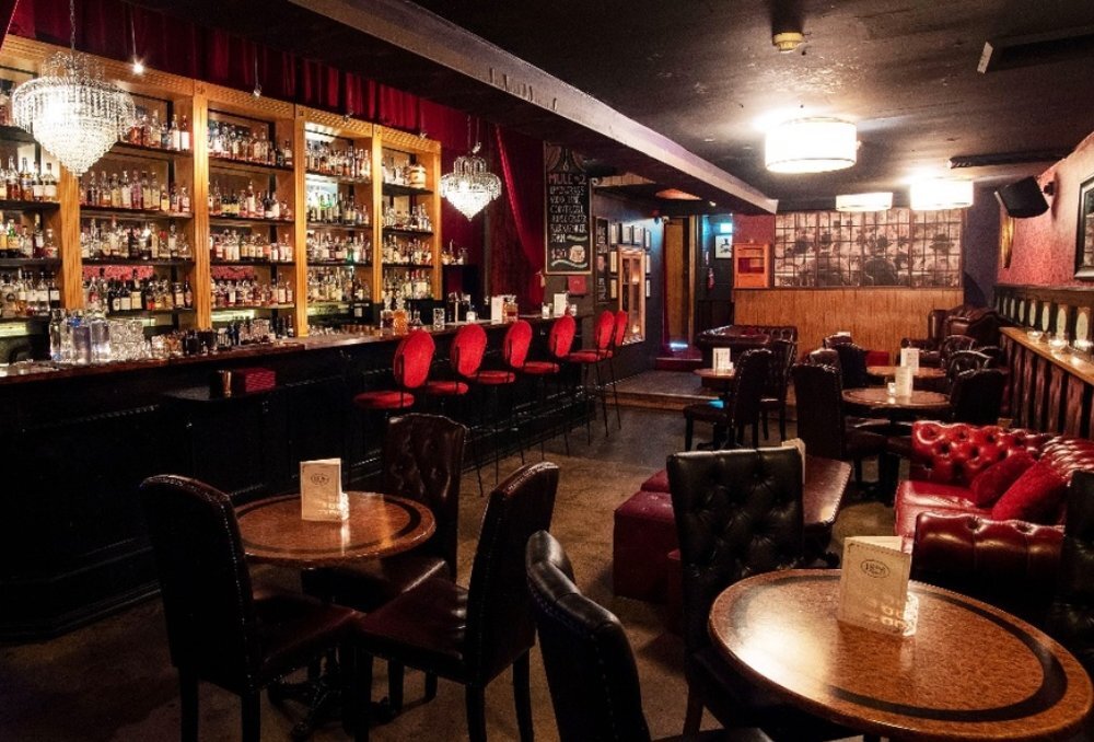 Dark bar with red chairs and lounges, and a well-stocked back bar.