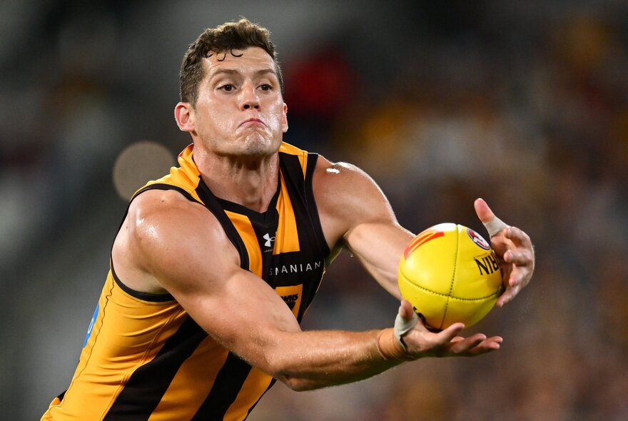 A  Hawthorn AFL football player marking the ball with his two hands in front of his chest, while running during a match.